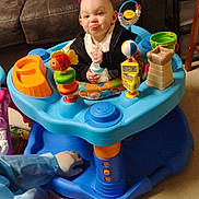 Dorothy is registered to the contest to win money with this photo: activity_center, baby, blue, bottle, carpet, child, clothing, colorful, couch, floor, furniture, hand, indoor, infant, person, playtime, room, smiling, tongue_out, toy