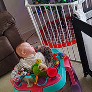 Isabella joined the competition — help win amazing prizes! baby, walker, toys, christmas_tree, ornaments, lights, indoor, floor, safety_gate, sofa, blanket, holiday, sleeping, infant, play_area, colorful, festive, toddler, home, relaxing