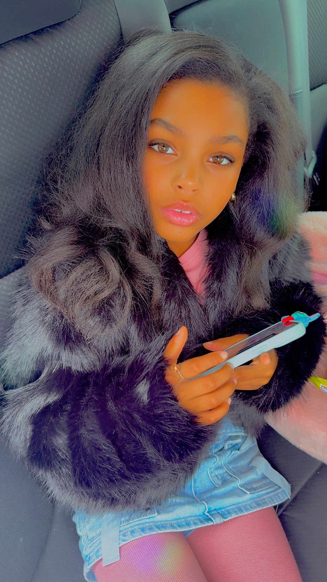 Reya joined the competition — help win amazing prizes! child, girl, phone, car_seat, denim_skirt, fur_jacket, long_hair, hands, pink_tights, portrait, casual_clothing, seat_belt, indoor, looking_at_camera, mobile_phone, fashion, young_person, sitting, face, brown_eyes