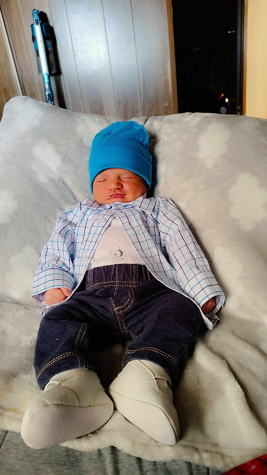 Kain is registered to the contest to win money with this photo: baby, blanket, blue_hat, checkered_shirt, child, clothing, comfortable, cozy, cute, dark_pants, indoors, infant, newborn, peaceful, portrait, resting, sleeping, soft_texture, white_booties, wood_paneling