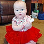 Sadie Dawn is registered to the contest to win money with this photo: baby, child, tutu, red_skirt, strawberry_shirt, carpet, sitting, indoor, blue_eyes, leather_couch, wooden_table, toy, curious, cross_legged, living_room, floor_mat, furniture, person, cute, infant