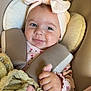 baby, infant, car_seat, headband, bow, pink, blanket, toy, braided_toy, clothing, straps, face, hand, smiling, child, seat, safety, closeup, indoor, warning_label