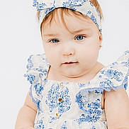 Skyla is registered to the contest to win money with this photo: baby, child, girl, headband, blue_eyes, dress, floral_pattern, cute, portrait, infant, fashion, white_background, soft_lighting, closeup, hands, face, eyewear, earrings, smile, innocence