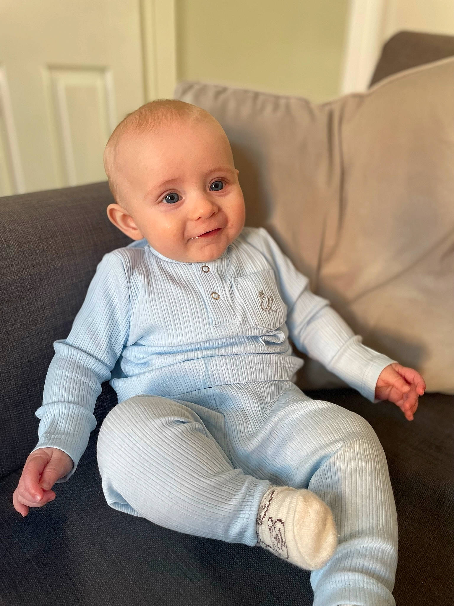 Connell is registered to the contest to win money with this photo: baby, baby_toddler_clothing, cheek, child, chin, comfort, couch, eye, face, finger, flooring, head, human_leg, iris, knee, person, sitting, skin, sleeve, smile