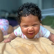 Safiya joined the competition — help win amazing prizes! baby, child, curly_hair, face, funny_expression, blanket, indoor, person, infant, crawling, cute, skin, clothing, hand, lying_down, soft, bedroom, blurred_background, toddler, room