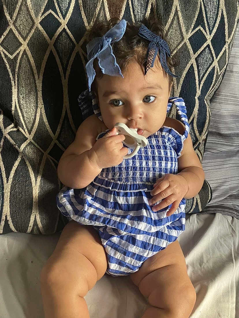 Jahnova is registered to the contest to win money with this photo: baby, child, pacifier, blue_bow, curly_hair, striped_outfit, pillow, patterned_background, sitting, indoors, cute, chubby, infant, hand, face, eyes, legs, skin, comfort, portrait