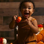 Emir is registered to the contest to win money with this photo: toddler, child, pumpkin, autumn, fall, orange, brown_clothing, happy, smiling, indoor, decor, seasonal, cute, person, baby, kneeling, curly_hair, bracelet, toy, warm_lighting