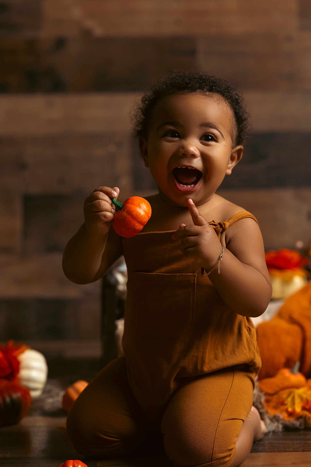 Emir is registered to the contest to win money with this photo: toddler, child, pumpkin, autumn, fall, orange, brown_clothing, happy, smiling, indoor, decor, seasonal, cute, person, baby, kneeling, curly_hair, bracelet, toy, warm_lighting