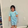 barefoot, blue_clothing, carpet, child, crayon_drawing, doorway, electrical_outlet, family_photo, happy, home, indoors, light_switch, pajamas, playful, portrait, smiling, standing, toddler, toys, wall