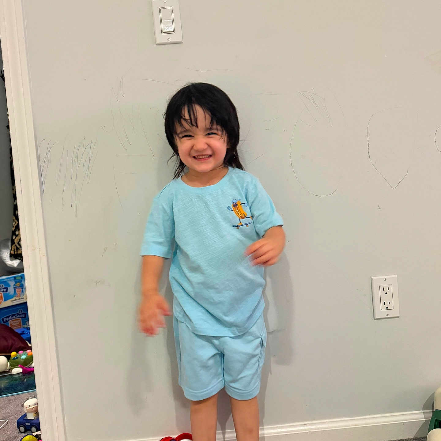 Omina is registered to the contest to win money with this photo: barefoot, blue_clothing, carpet, child, crayon_drawing, doorway, electrical_outlet, family_photo, happy, home, indoors, light_switch, pajamas, playful, portrait, smiling, standing, toddler, toys, wall