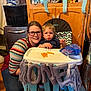 Jayden is registered to the contest to win money with this photo: balloon, banner, birthday, blue_streamers, cabinet, celebration, cheese_puffs, child, decorations, floor, food, glasses, high_chair, kitchen, party, person, shoe, smile, snack, woman