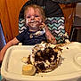 Jayden is registered to the contest to win money with this photo: birthday, cabinet, cake, child, chocolate_cake, clothing, expression, face, food, frosting, hair, hand, high_chair, indoor, messy, person, seat, table, toddler, young_child