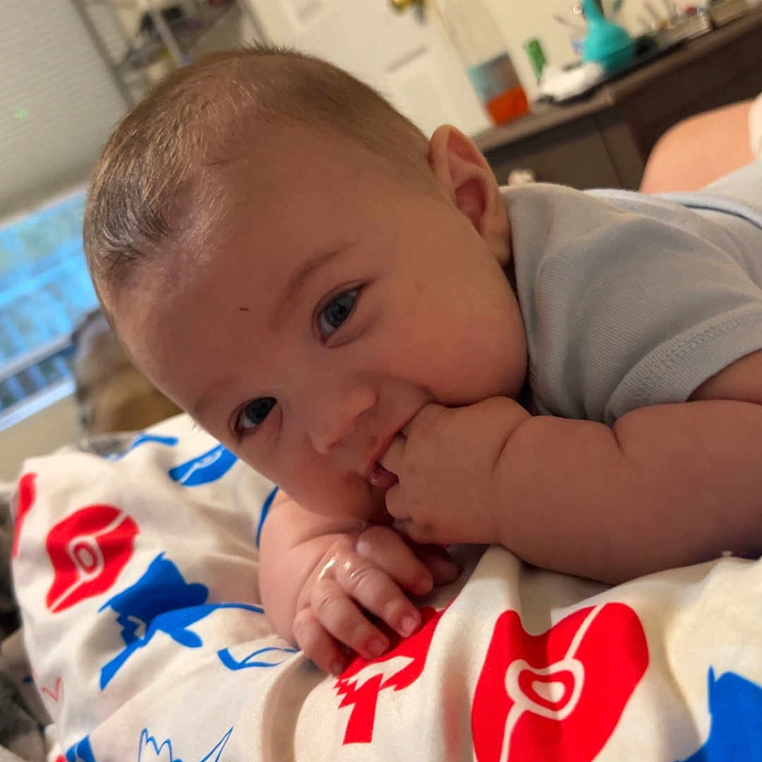 Zayden is registered to the contest to win money with this photo: baby, blanket, blue_eyes, child, closeup, colorful, curious, door, face, fingers, hand, indoor, infant, lying_down, patterned_blanket, room, shelf, short_hair, soft_toy, toy