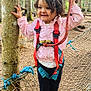 child, girl, forest, rope_net, harness, safety_gear, pink_jacket, curly_hair, smiling, outdoor, trees, adventure_park, footwear, pink_bows, playground, nature, young_child, happy, rope, balance