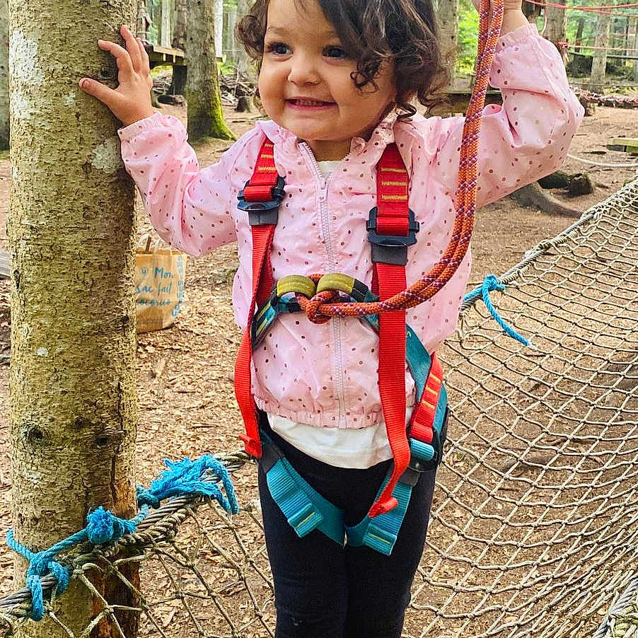 Syrine a rejoint le concours — aidez-le/la à gagner de superbes lots ! adventure_park, balance, child, curly_hair, footwear, forest, girl, happy, harness, nature, outdoor, pink_bows, pink_jacket, playground, rope, rope_net, safety_gear, smiling, trees, young_child