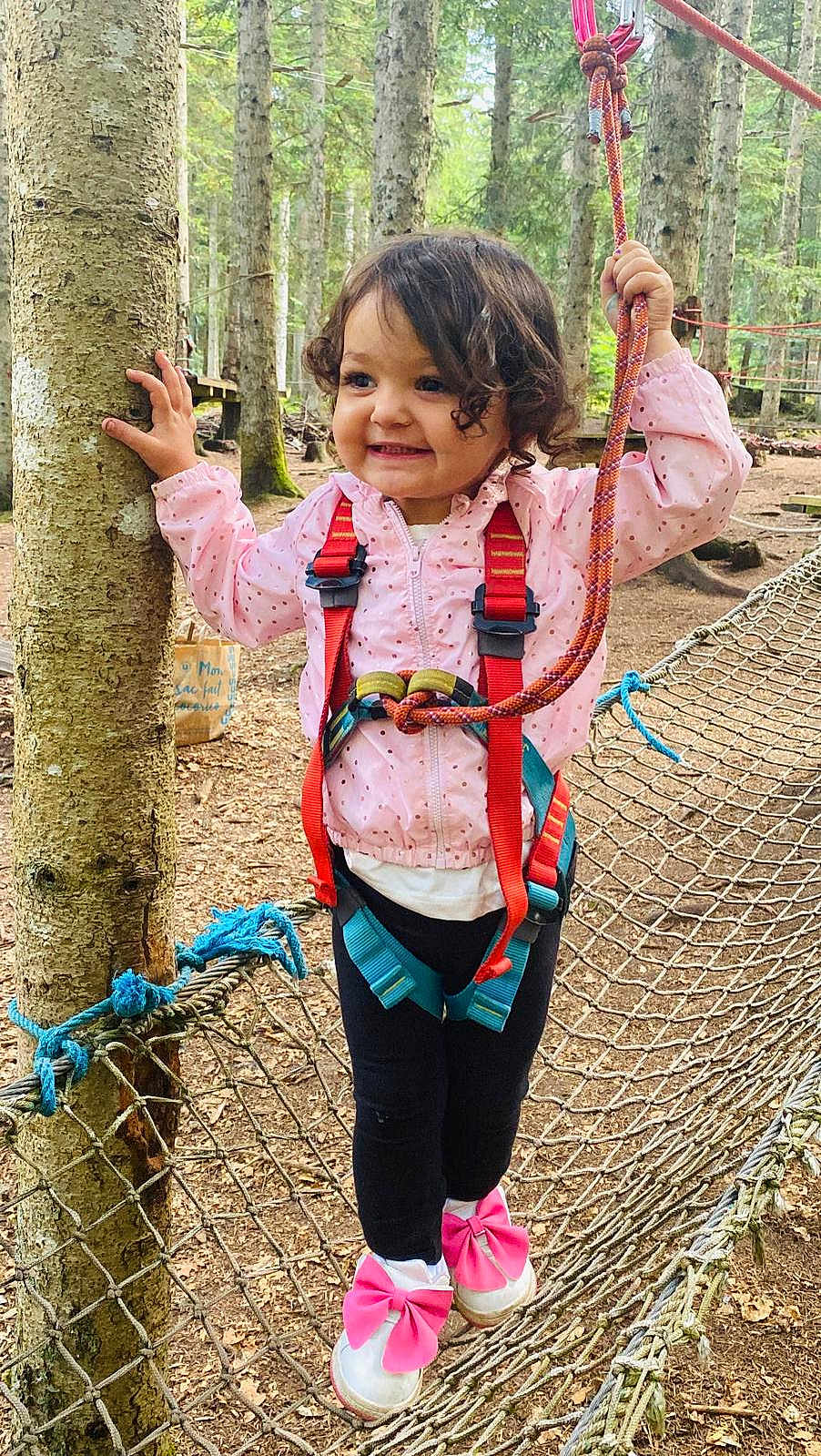 Syrine a rejoint le concours — aidez-le/la à gagner de superbes lots ! child, girl, forest, rope_net, harness, safety_gear, pink_jacket, curly_hair, smiling, outdoor, trees, adventure_park, footwear, pink_bows, playground, nature, young_child, happy, rope, balance