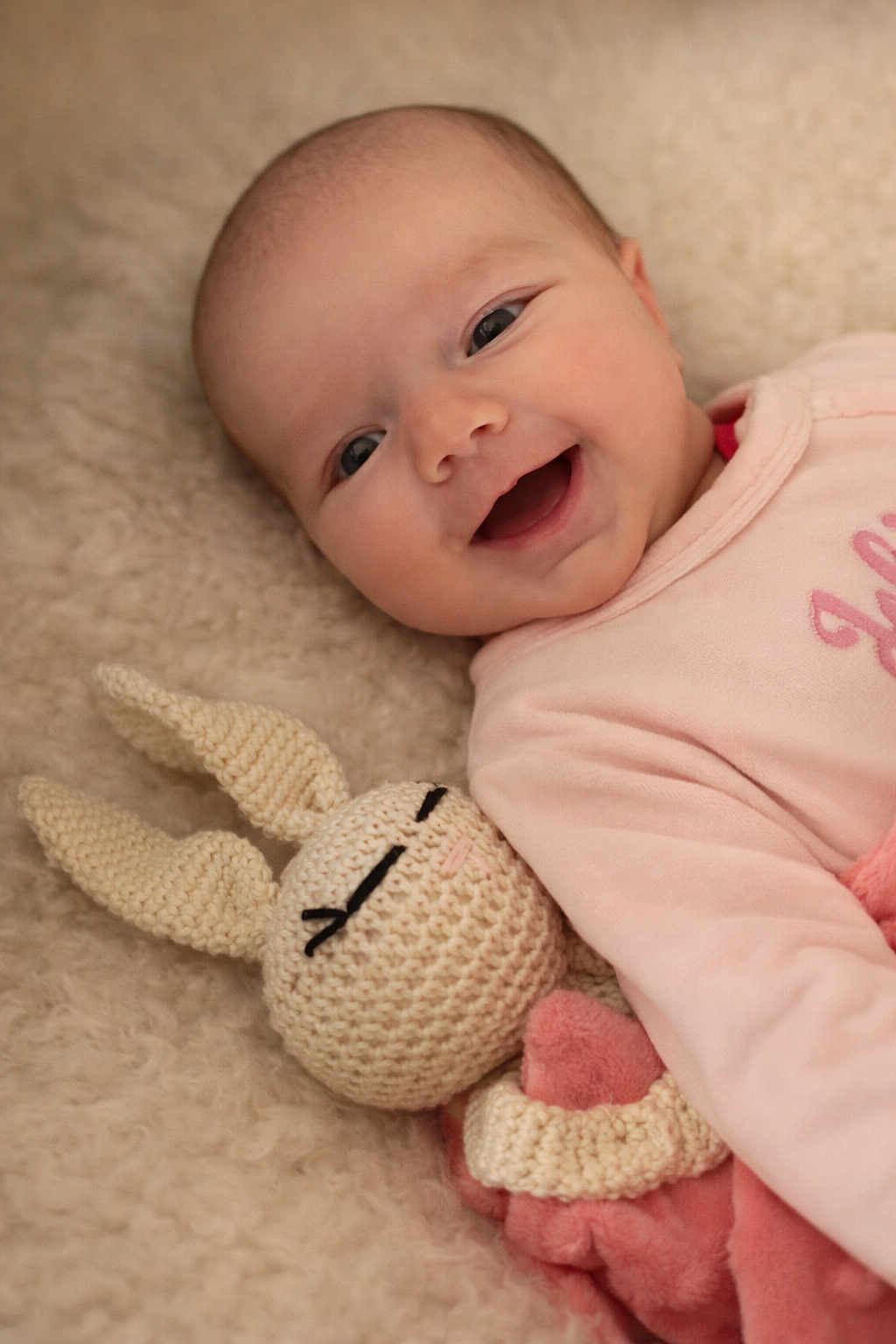Mia participe au concours pour gagner de l'argent avec cette photo : baby, smiling, infant, knitted_toy, bunny, soft_texture, blanket, pink_clothing, cute, happy, lying_down, cozy, child, toddler, plush_toy, face, closeup, indoor, portrait, snuggling