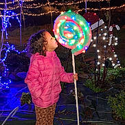 Charlie participe au concours pour gagner de l'argent avec cette photo : child, pink_jacket, lollipop_prop, string_lights, night, outdoor, holiday_lights, curly_hair, sneakers, patterned_pants, festive, garden, decorations, toy, stick, illumination, display, grass, curiosity, portrait