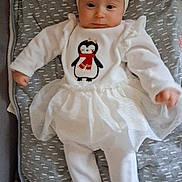 Louise participe au concours pour gagner de l'argent avec cette photo : baby, infant, newborn, headband, bow, penguin_embroidered, onesie, tutu, white_clothing, blanket, swaddle, smile, face, eyes, hands, legs, plush_toy, couch, cozy, portrait