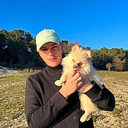 Thanos participe au concours pour gagner de l'argent avec cette photo : animal, blue_sky, cap, casual, cute, daylight, dog, fluffy, grass, holding, man, nature, outdoor, pet, portrait, smile, sunlight, sweater, trees, young_adult