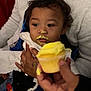 Tyce is registered to the contest to win money with this photo: child, baby, cupcake, frosting, yellow_frosting, face, hand, adult, clothing, jeans, sitting, holding, food, messy, indoor, person, napkin, celebration, curious, closeup