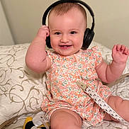 Aitana joined the competition — help win amazing prizes! baby, headphones, smiling, floral_dress, plush_toy, bed, blanket, infant, cute, happy, indoors, child, person, sitting, toy, playful, candid, soft_lighting, closeup, expression