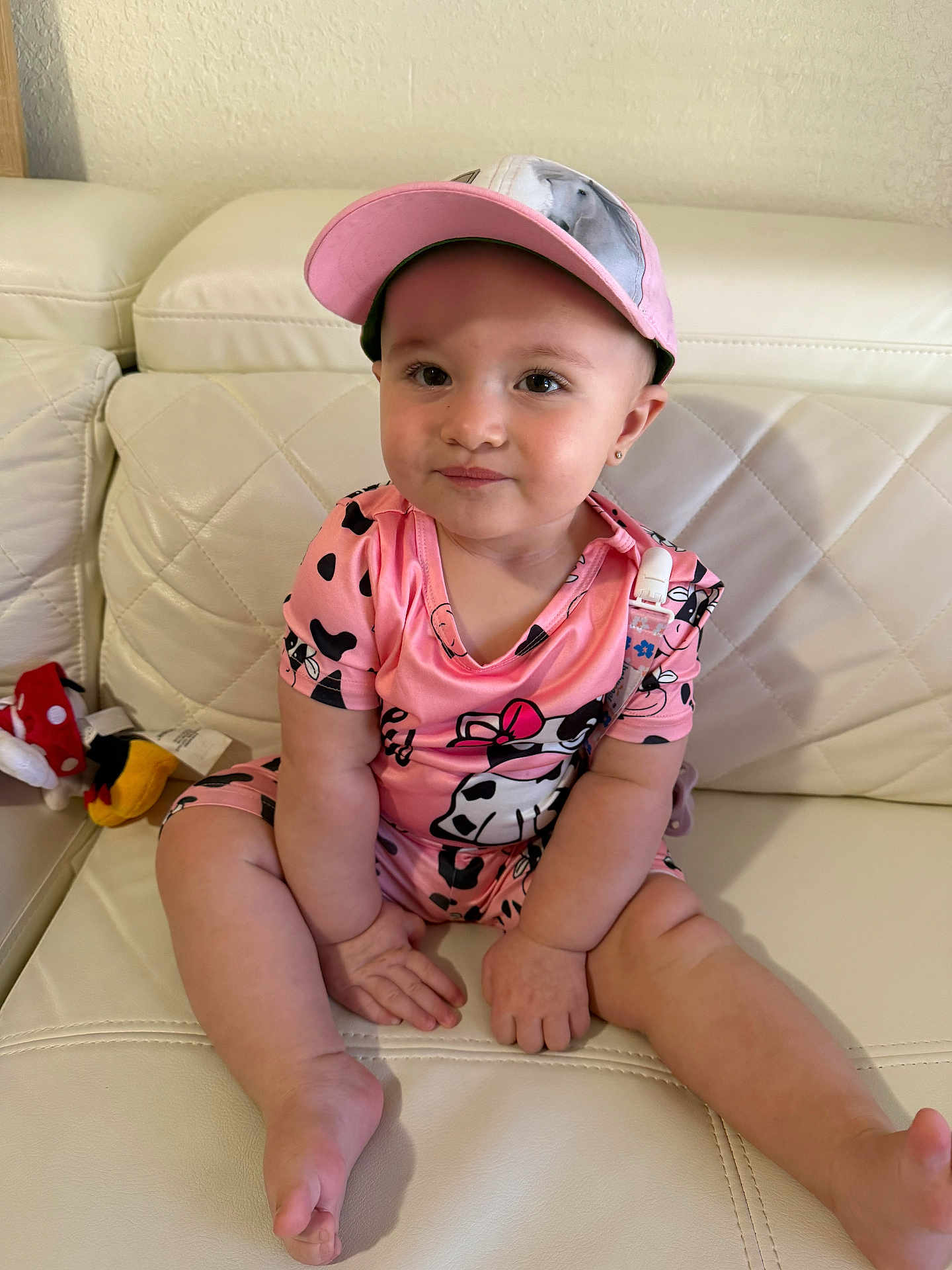 Aitana is registered to the contest to win money with this photo: toddler, child, baby, pink_clothing, cap, sitting, couch, white_leather, indoor, cute, smile, face, person, toy, relaxed, legs, hands, headwear, casual, cozy