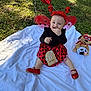 Aitana is registered to the contest to win money with this photo: baby, child, outdoor, grass, blanket, ladybug_costume, red_shoes, balloons, plush_toy, smiling, wings, headband, costume, sitting, cute, happy, infant, celebration, nature, toy
