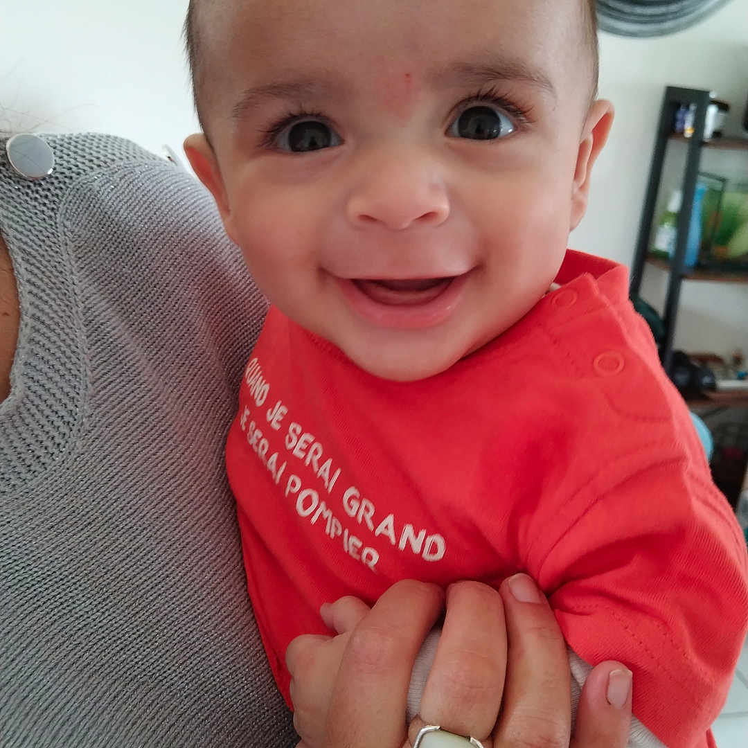 Tyam participe au concours pour gagner de l'argent avec cette photo : adult_hand, baby, casual, child, clock, eyes, face, furniture, hand, happy, holding, home, indoor, person, portrait, red_clothing, shelf, skin, smiling, sweater