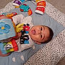 baby, child, play_mat, toy, soft_toy, colorful, smiling, happy, indoors, carpet, clothing, person, face, head, infant, cute, playtime, cushion, patterned, toddler