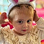 child, toddler, bunny_ears, costume, cream_sweater, frills, portrait, indoors, cute, curious, face, person, young_child, soft_lighting, closeup, baby, headwear, expression, fashion, playful