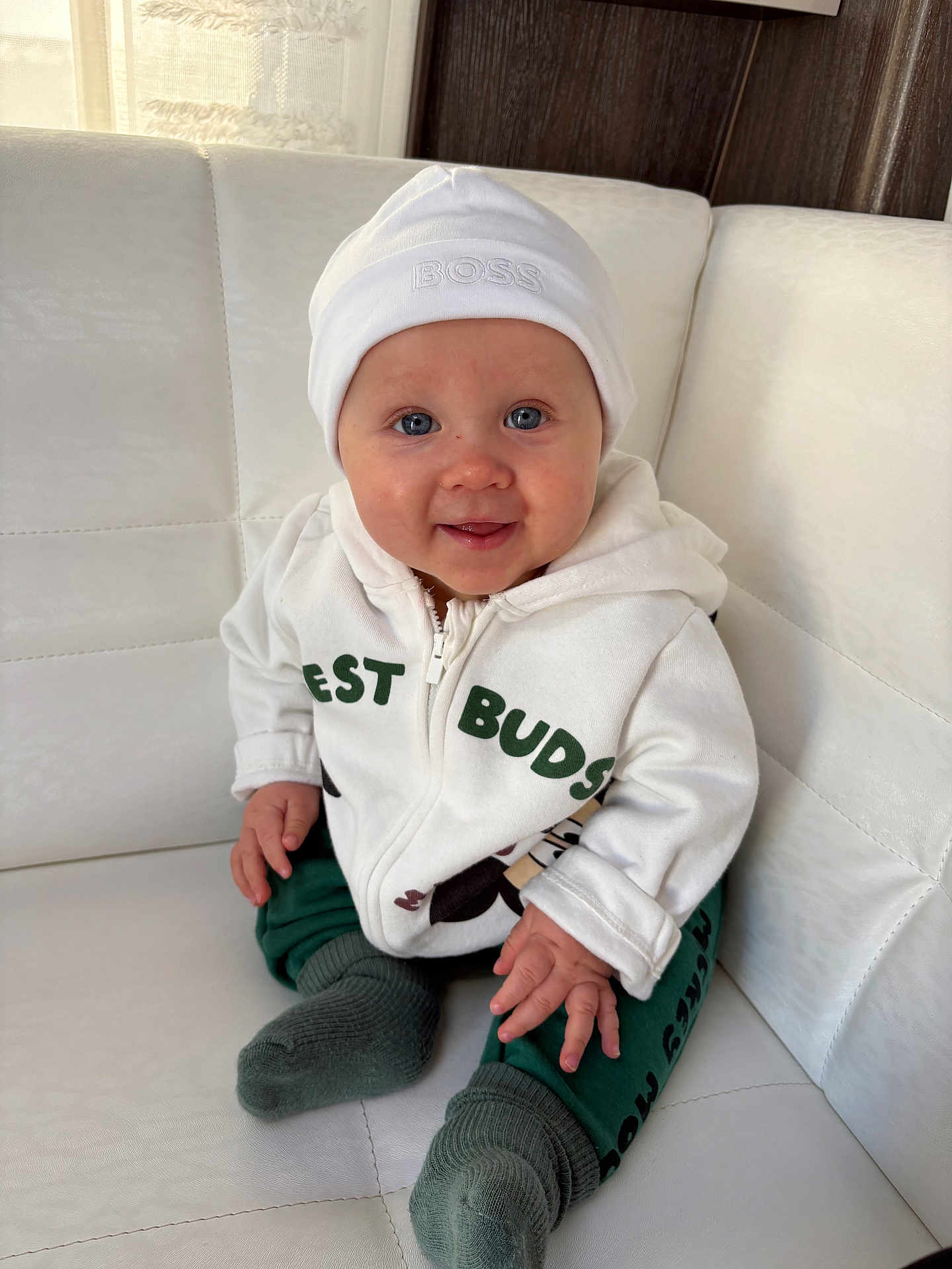 Eliakim participe au concours pour gagner de l'argent avec cette photo : baby, child, infant, smiling, white_hat, hoodie, green_pants, socks, sitting, couch, indoor, cute, happy, face, blue_eyes, person, clothing, cozy, portrait, home