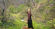 Yogi Bear is registered to the contest to win money with this photo: woman, dog, forest, nature, greenery, path, leash, outdoor, trees, grass, flowering_vines, bushes, sky, daytime, canine, walking, pet, scenic, casual_clothing, long_hair