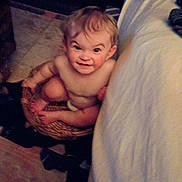 Jaxon is registered to the contest to win money with this photo: baby, basket, indoor, floor, blanket, carpet, child, smile, face, skin, hair, person, foot, hand, seated, expression, cozy, warm_lighting, room, furniture