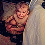 baby, basket, indoor, floor, blanket, carpet, child, smile, face, skin, hair, person, foot, hand, seated, expression, cozy, warm_lighting, room, furniture