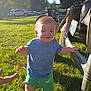 Jaxon is registered to the contest to win money with this photo: toddler, child, grass, vintage_car, blue_shirt, green_shorts, sunlight, outdoor, trees, car_bumper, hand, smile, walking, daytime, license_plate, parked_cars, playing, person, happy, baby
