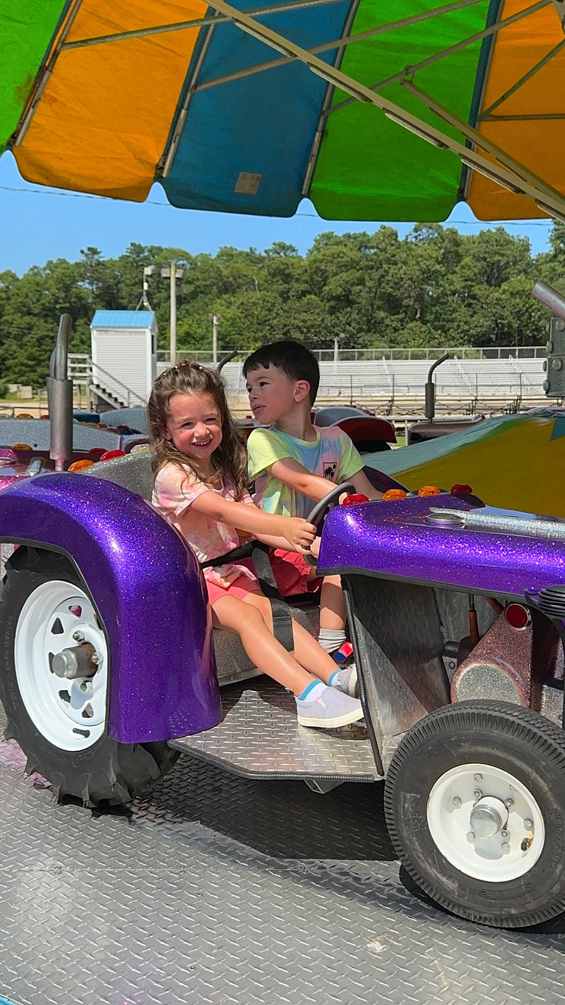 Emilia is registered to the contest to win money with this photo: automotive_exterior, automotive_tire, automotive_wheel_system, bumper, child, fun, grass, joy, leisure, motor_vehicle, person, public_space, recreation, rolling, shade, tire, travel, tread, tree, umbrella