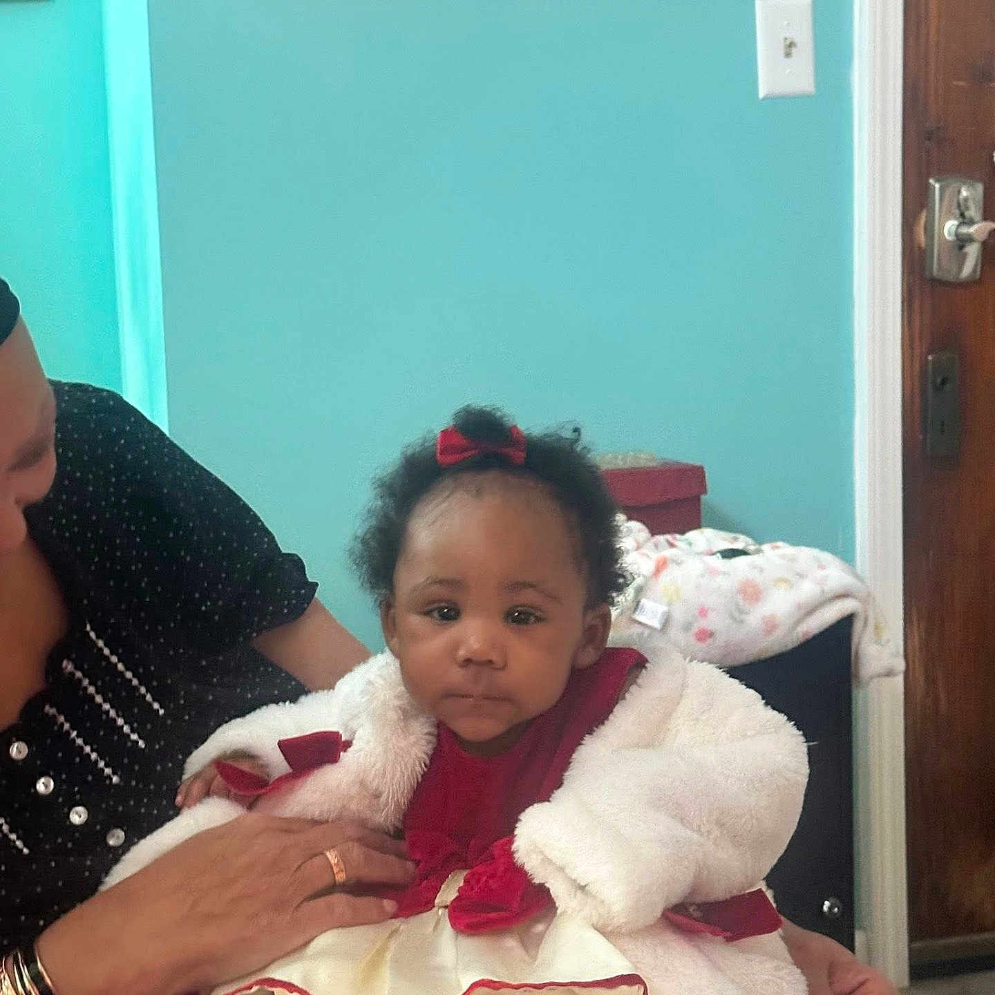Taniya joined the competition — help win amazing prizes! baby, child, infant, woman, adult, indoor, dress, coat, bow, red, white, teal_wall, painting, door, hand, person, furniture, floor, portrait, cute