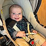 baby, smiling, stroller, plaid_shirt, beige, toy, indoor, child, happy, clothing, seatbelt, foot, hand, fabric, person, infant, cute, comfort, young, face