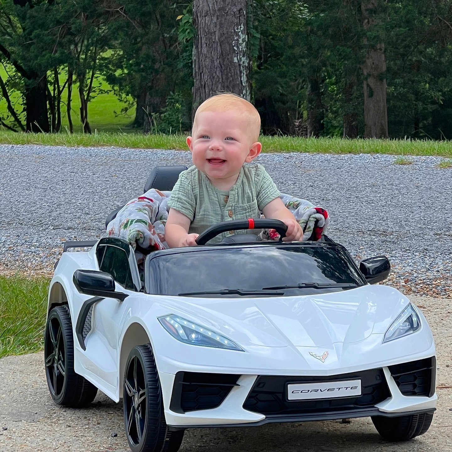 Jon Lewis joined the competition — help win amazing prizes! baby, blanket, child, corvette, cute, daylight, grass, happy, infant, nature, outdoor, playing, road, small_car, smiling, steering_wheel, toy_car, toy_vehicle, trees, white_car