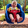 baby, child, swing, outdoor, playground, grass, trees, sunny, smiling, happy, blue_swing, red_safety_bar, yellow_straps, feet, rocks, golf_cart, greenery, daylight, person