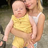 Kade is registered to the contest to win money with this photo: baby, child, sister, siblings, portrait, smiling, outdoor, family, holding, infant, blonde_hair, yellow_outfit, white_dress, arms, standing, photography, sunlight, background_blur, happy, family_moment