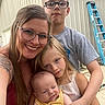 family, mother, children, baby, toddler, boy, girl, infant, smiling, portrait, selfie, outdoor, garage, workshop, ladder, eyeglasses, long_hair, tattoo, yellow_outfit, group_photo