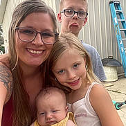 Khloe is registered to the contest to win money with this photo: family, mother, children, baby, toddler, boy, girl, infant, selfie, portrait, smiling, funny_face, outdoor, shed, ladder, grill, scooter, glasses, blonde_hair, group_photo