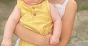 Khloe is registered to the contest to win money with this photo: baby, child, siblings, sister, portrait, holding, smiling, sleepy, outdoor, family, yellow_outfit, blonde_hair, infant, toddler, young_girl, arms, wooden_deck, patio, standing, photography