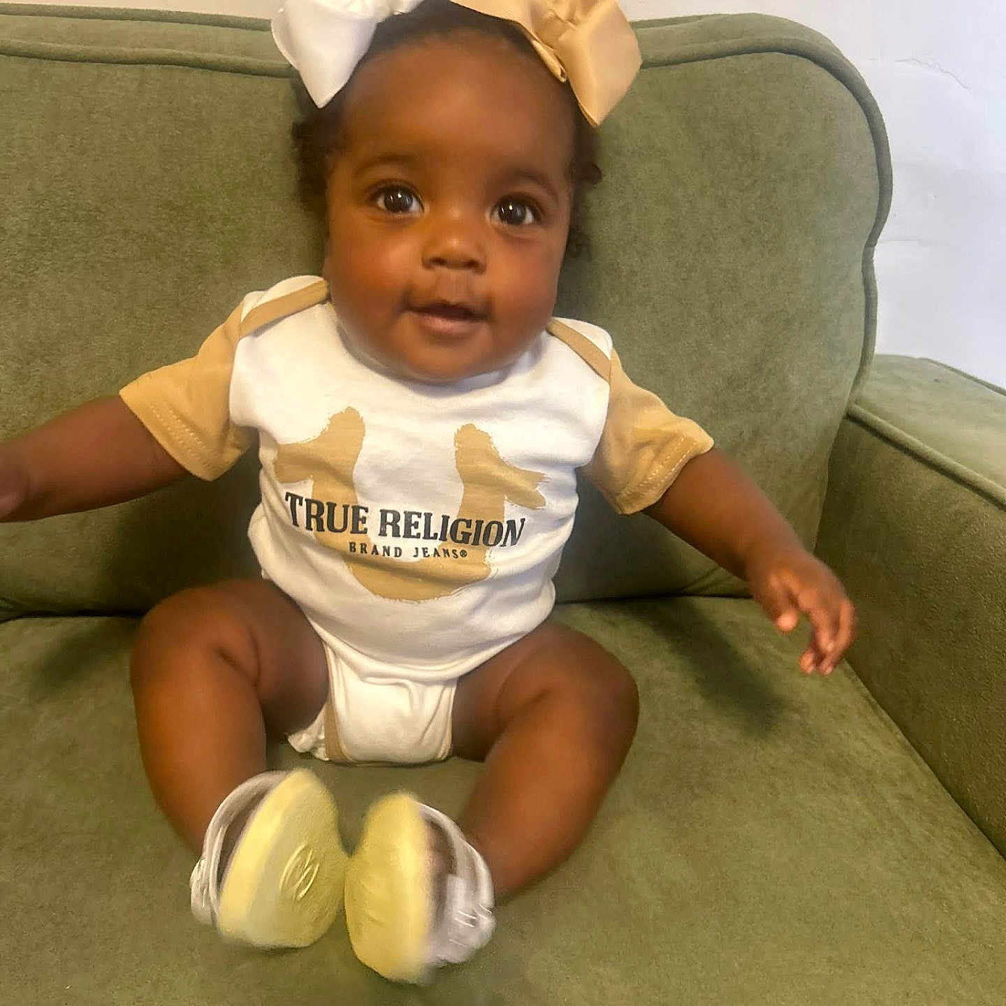 Gabriella joined the competition — help win amazing prizes! baby, child, bow, cute, couch, infant, indoors, person, portrait, sitting, smiling, clothing, footwear, furniture, green, happy, headwear, young_child, skin, eyes