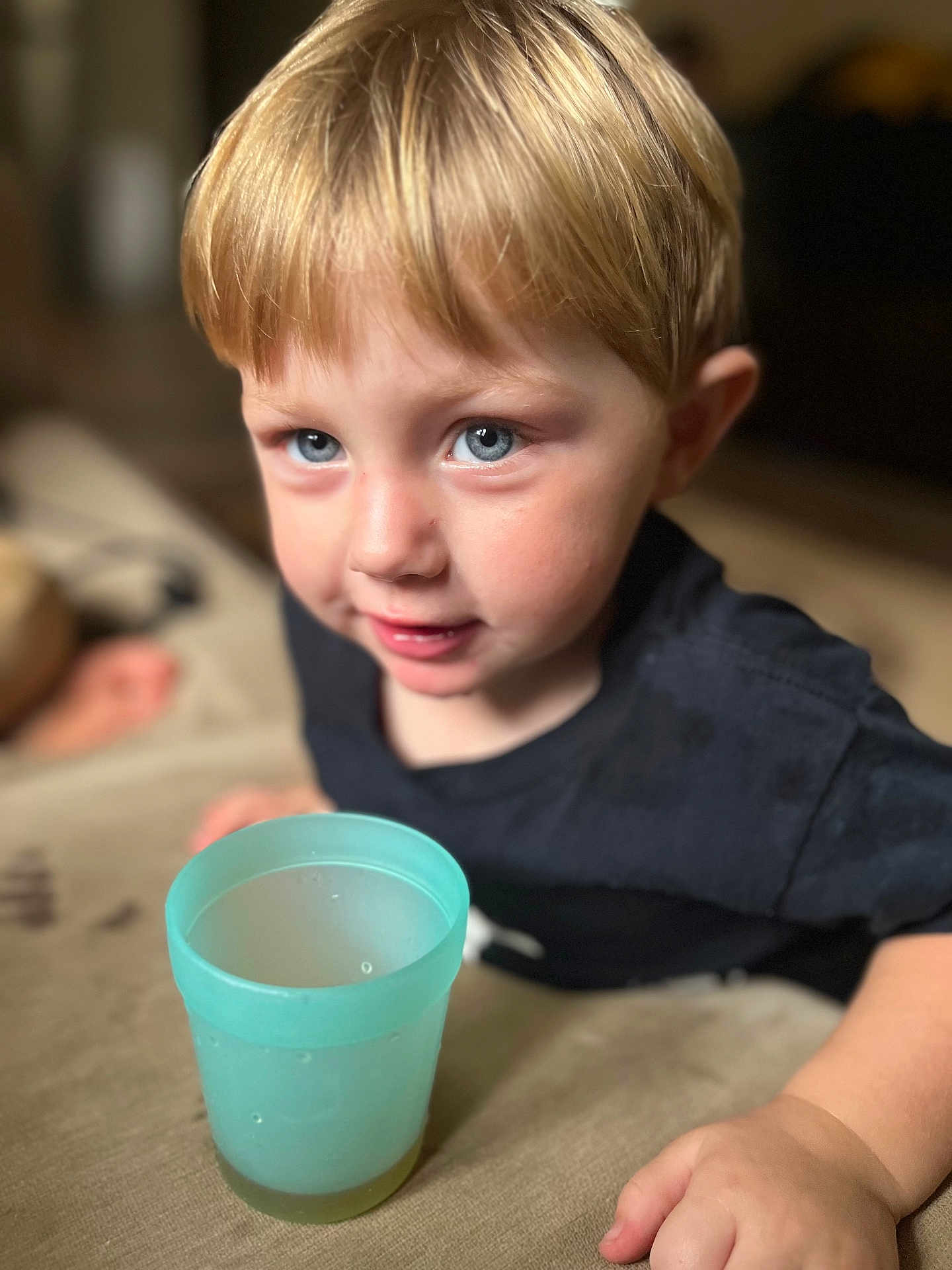 Grayson is registered to the contest to win money with this photo: child, toddler, blond_hair, blue_eyes, portrait, close_up, indoor, plastic_cup, drink, hand, couch, shallow_depth_of_field, casual_clothing, cute, curious, smiling, gaze, domestic, young_boy, bokeh