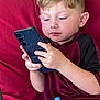 Grayson is registered to the contest to win money with this photo: child, boy, smartphone, sippy_cup, red_cushion, maroon_shirt, sitting, hands, face, blond_hair, ears, portrait, indoor, concentration, casual_clothing, close_up, couch, technology, relaxed, toddlers_item