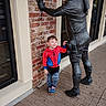 child, boy, statue, brick_wall, sidewalk, building, window, spiderman_hoodie, smiling, outdoor, casual_clothing, footwear, toy_shoes, playful, happy, daylight, urban, posing, person, sculpture