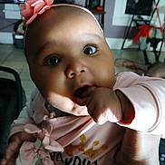 Modestie joined the competition — help win amazing prizes! baby, infant, pink_headband, flower, hand, fingers, face, eyes, clothing, indoor, floor_tile, television, furniture, person, cute, portrait, child, sitting, home, family